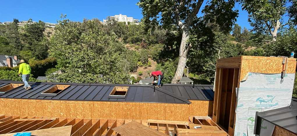 Two roofers installing metal panels across an active framed roof.